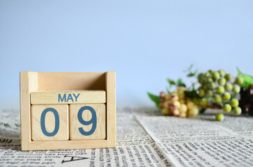 May 9, Calendar cover design with number cube with fruit on newspaper fabric and blue background.