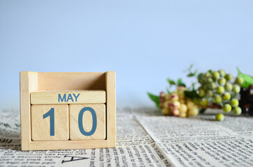 May 10, Calendar cover design with number cube with fruit on newspaper fabric and blue background.