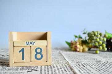 May 18, Calendar cover design with number cube with fruit on newspaper fabric and blue background.