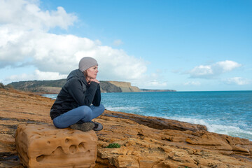 woman sitting on a rock watching the waves, sorrowful, alone concept