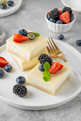 Vanilla cheesecake cut into squares with fresh berries on a white plate on a gray stone background