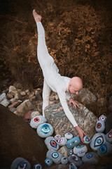 Flexible hairless girl with alopecia in white futuristic costume put her foot up and reaches hand...