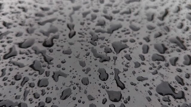 rain drops on black car bonnet surface, closeup with slow motion