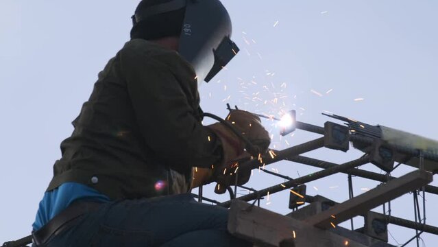 Industrial welder welding fabricated construction stick welding. Worker in helmet performs welding work at height.
