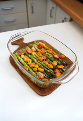 Green asparagus baked with tomatoes and cheese in a baking dish on a cutting board