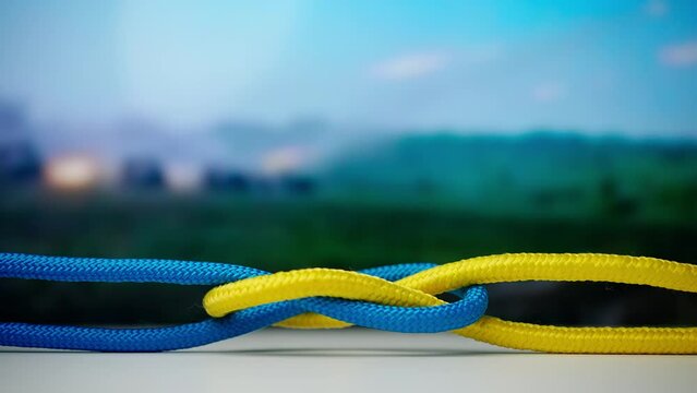 Yellow and blue colored ropes twisted and tied up creating knot against background with digital screen showing military and war media content.
