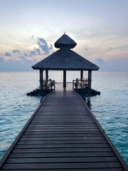 Pier of Maldivian resort at sunrise or sunset, vertical photo 
