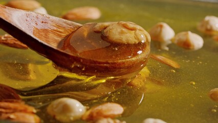 Wooden spoon scooping sweet fresh golden honey with almonds, walnuts and hazelnuts in the thick...