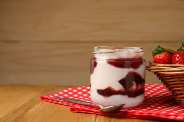 Tasty yoghurt with jam, spoon and strawberries on wooden table, closeup. Space for text