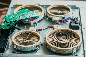 Electric cooktop lies disassembled, revealing its intricate circuit board and heating elements,...