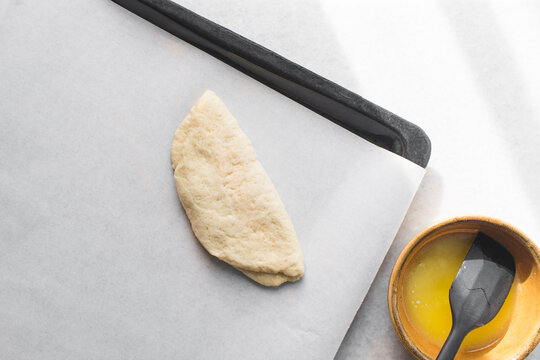 Coco bread dough rising on a parchment lined baking tray, shaped coco bread about to be baked, process of making jamaican coco bread