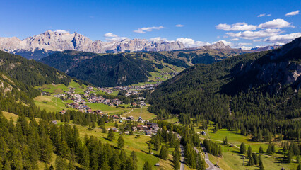 Amazing drone view of  idyllic landscape in the Dolomites with fresh green meadows, cozy village houses and majestic mountain peaks.