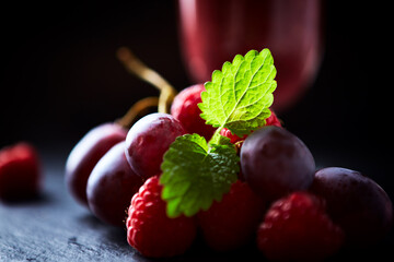 Grapes and raspberries and fresh smoothie in a glass. Dark background. Close up.
