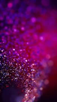 Glowing small particles swirl around on a purple background. Holiday looping animation with bokeh effect. Flickering bright sparks. Vertical video.