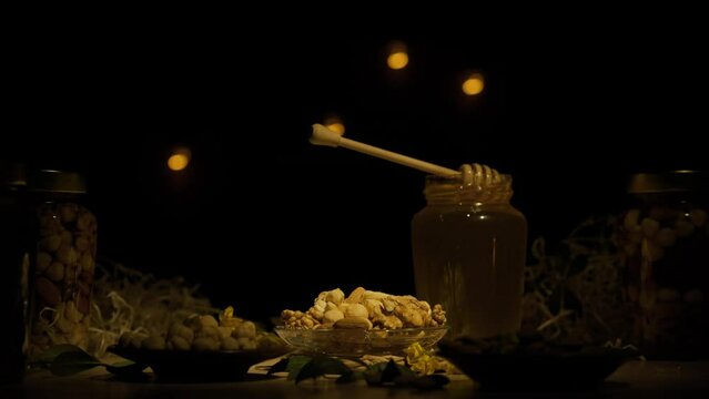 Glass jars standing on the wooden table with fresh golden honey, honey dipper laying on the open jar in the thick syrup, dark background.