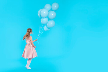 girl in pink dress with balloons running on blue background   with copy space