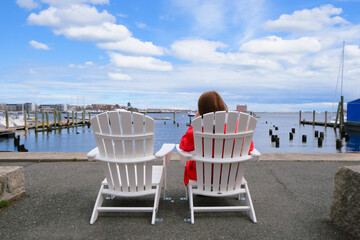 woman sitting on the beach chair next to free chair at the pier watching bay and cloudy sky, relax...