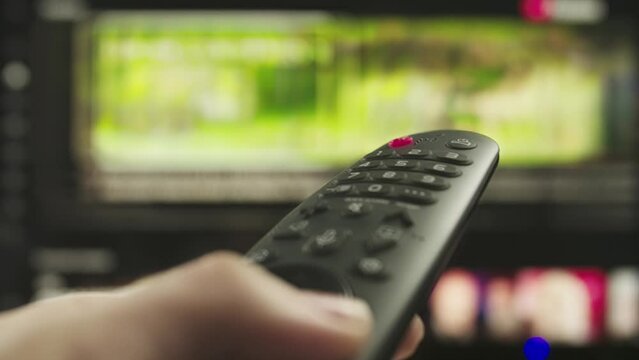 Man with remote in hand switching channels, smart tv technology internet video content, screen with movie content at the background close up shot.