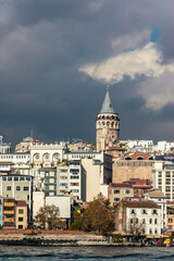 Fototapeta na wymiar The Galata Tower stands tall amidst the modern Istanbul skyline under a dramatic cloud-filled sky. Istanbul, Turkey (Turkiye)