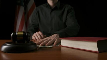 Law and justice. Male sitting at the desk with wooden hammer and law book, USA flag at the...