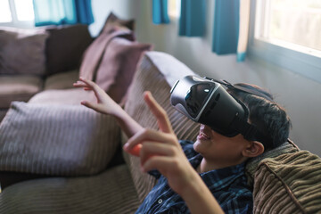 Young kid immerse within the Virtual reality world wearing VR headset gaming and entertainment having fun. At home living room relaxing on sofa online internet device technology concept.