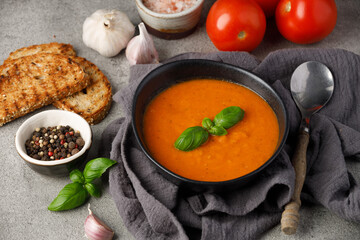 Classic tomato soup with basil and dried green herbs on a gray background