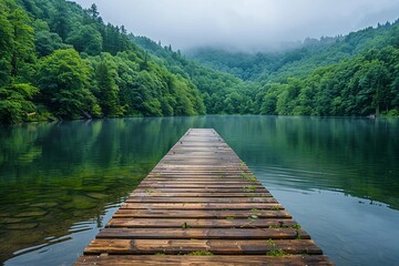 A calming waterfront view, inviting one to relax on a wooden dock leading to a serene lake surrounded by lush green forests copy space for text
