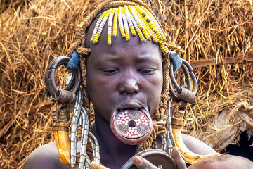 Ethiopia, a woman from the Mursi tribe with beautiful head decoration sits in front of her hut. Omo...