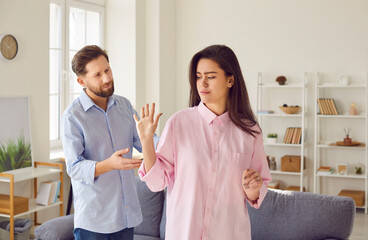 Emotionally stressed young couple arguing angrily at home during family conflict. Girl shows contemptuous gesture and her facial expression hints at irritation and refusal to further interact with man