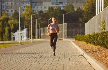 Female young runner jogging alone in city park. Healthy sporty fitness woman running outdoors...