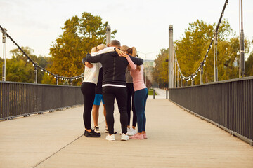 Group of friends having an outdoor city workout together. Team of people standing on a bridge and hugging. Teamwork, fitness, sport, exercise, wellness, healthy lifestyle concept