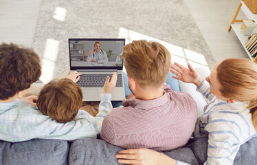 Young family having online telemedicine consultation on a laptop with their pediatrician doctor sitting on the sofa with two boys children having seasonal flu or cold in the living room at home. - 796956766