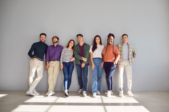 Group studio portrait, young diverse graduate students, college friends full length wall standing. People wearing smart casual wear, posing for graduation album, friendly smiling, healthy adult life