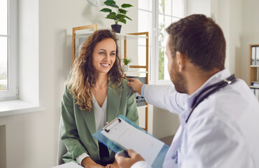Portrait of a male doctor support young smiling female patient putting hand on her shoulder. Physician sitting in medical clinic giving consultation a woman during medical examination in office. - 796959929