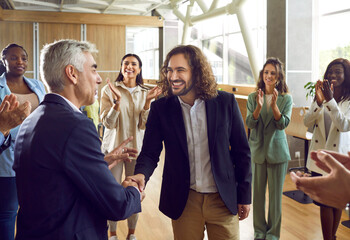 Nice work, young man. Diverse business team celebrating colleague's successful job promotion and having fun together. Smiling boss exchanges handshakes with happy employee while others clap hands - obrazy, fototapety, plakaty