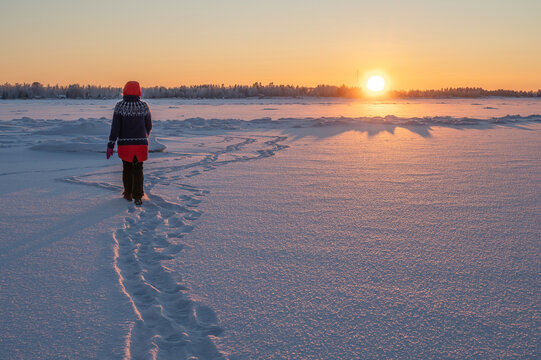 woman walking on the frozen sea towards the sunset. Finland