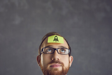 Close up shot of young man looking at his forehead with yellow with picture of space rocket. Concepts of business, innovation, creative thinking and planning new project - 796973337
