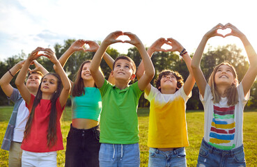 Happy children making heart shapes with their hands raised. Group of smiling boys and girls playing on nature outdoors in sunny day. Kids joining hands in shape of hearts expressing love - 796977337