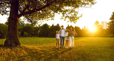 Happy smiling family of four with two kids boy and girl walking in summer park enjoying beautiful nature. Young parents and their children hugging outdoors enjoying time together. Banner. - 796977981
