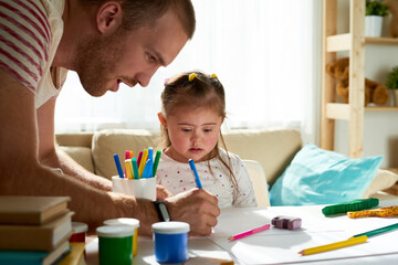 Portrait of cute little girl with Down syndrome painting with father assisting, copy space
