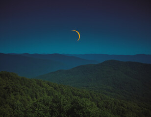 Thin Crescent Moon in a Starry Night Sky Over a Forested Landscape