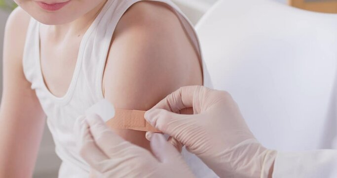 Doctor, family physician, pediatrician in medical gloves gluing med patch on kid hand after injection, finishing anti covid vaccination in clinic, child, children healthcare concept, close up