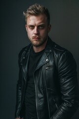 Obraz premium Confident young man in a leather jacket posing against a dark background