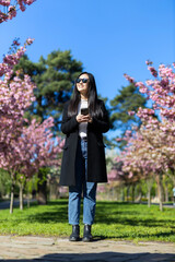 A Korean or Japanese woman relaxes under blooming sakura in the springtime park, embodying natural beauty.