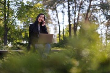 In the park, a Korean or Japanese woman enjoys nature while working on her laptop, staying...