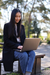 Japanese businesswoman works on her laptop in the park, exuding professionalism and focus.