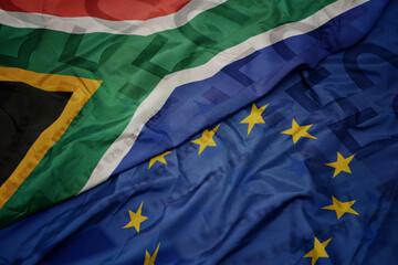 waving colorful flag of european union and flag of south africa on a euro money banknotes background. finance concept.