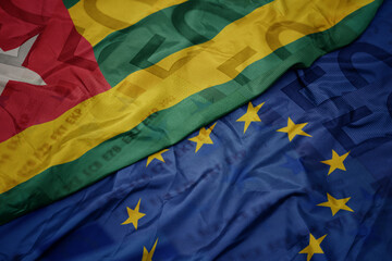 waving colorful flag of european union and flag of togo on a euro money banknotes background. finance concept.