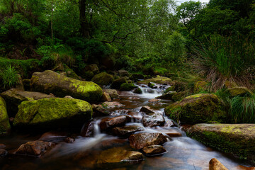 Naklejka na ściany i meble Water streaming over rocky cascades, Deep forest waterfall small waterfall with blurred water on the rocks in the peak district uk
