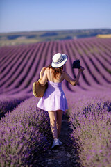 A woman wearing a white hat and a purple dress walks through a field of lavender. The scene is serene and peaceful, with the woman enjoying the beauty of the flowers and the fresh air.